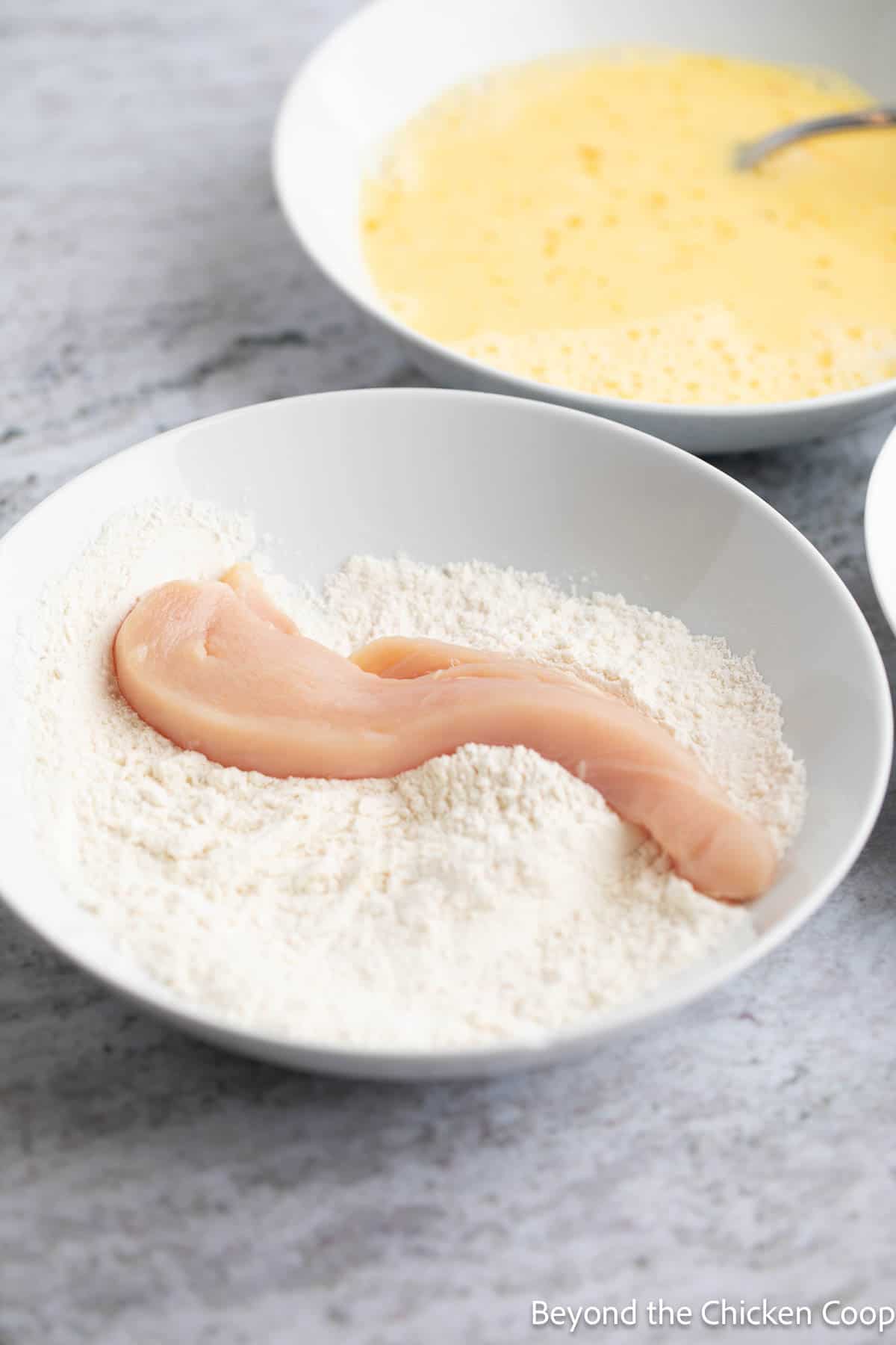 A chicken strip in a bowl with flour. 