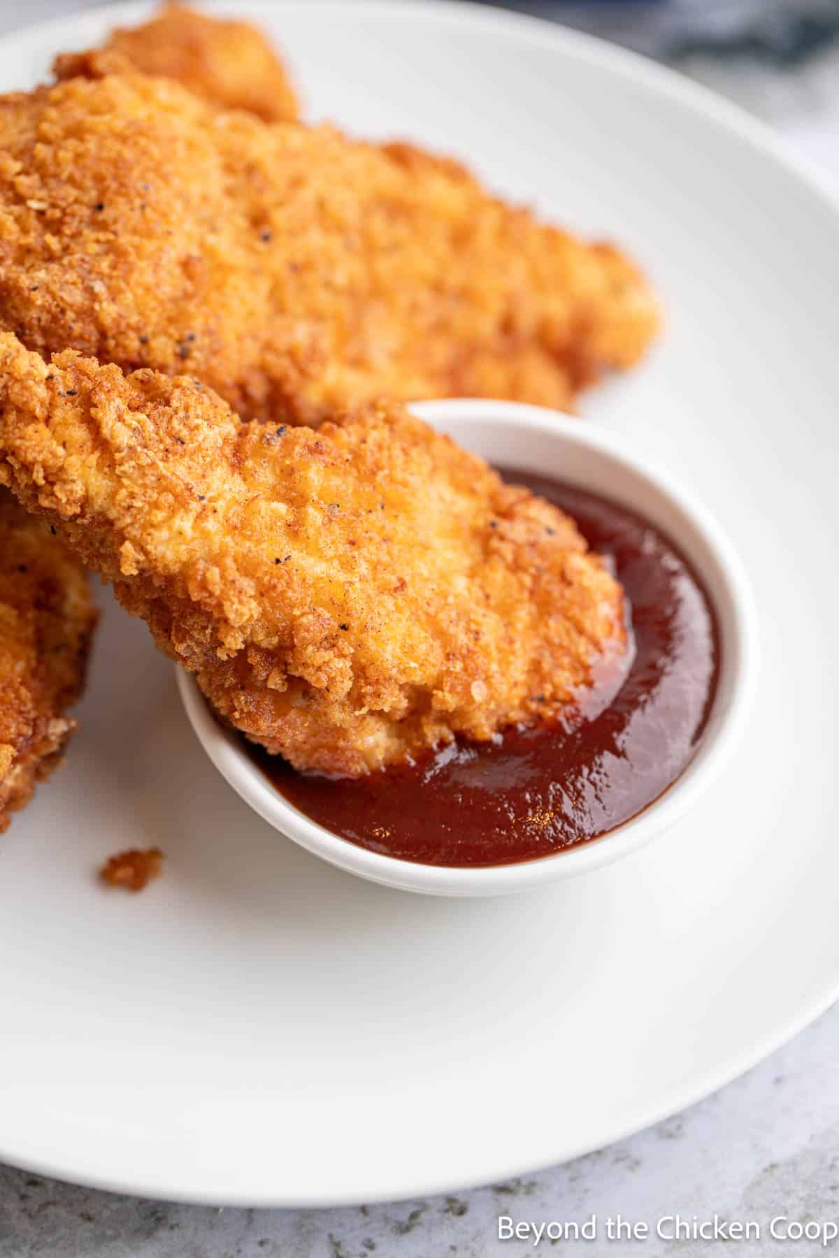 Chicken strip dunked into a bowl of BBQ sauce. 