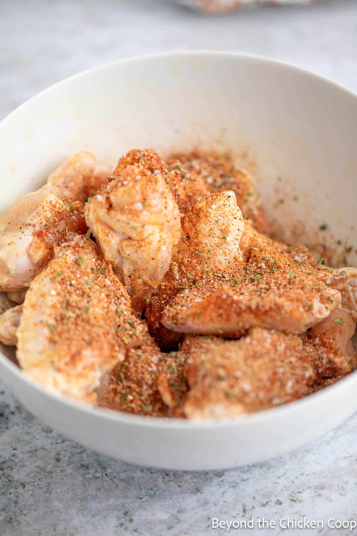 Seasoning sprinkled over a bowl of chicken wings. 