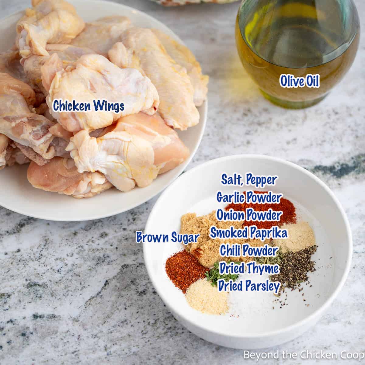 Chicken wings and a bowl filled of spices next to a bottle of olive oil. 