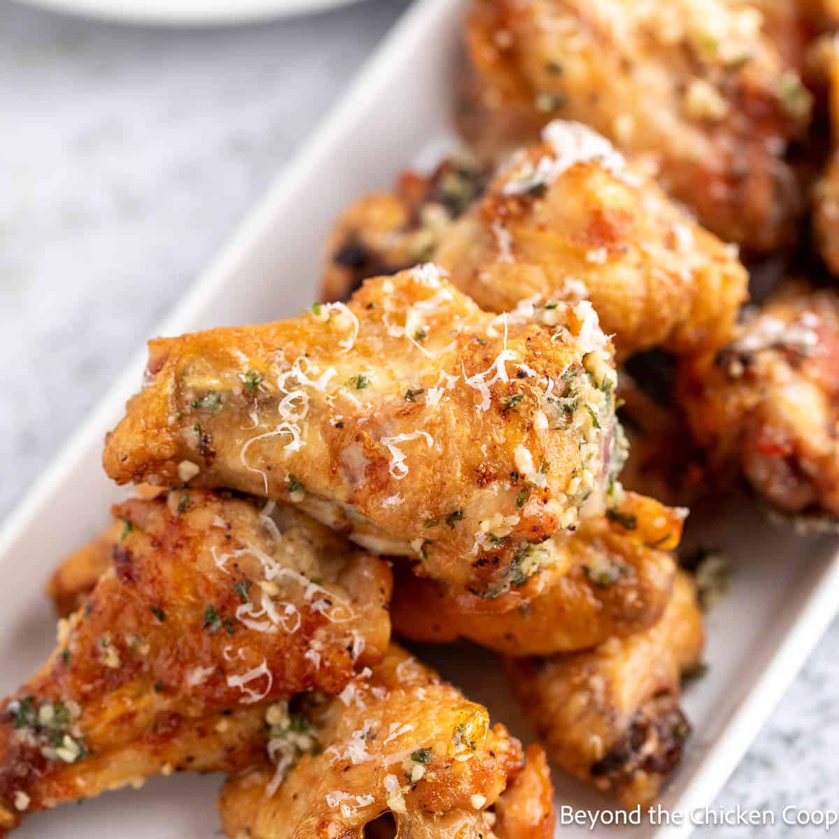 Garlic Parmesan wings stack on a white platter. 