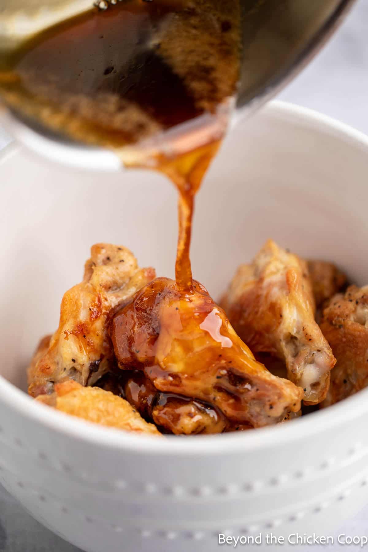 Pouring a hot honey sauce over baked chicken wings. 