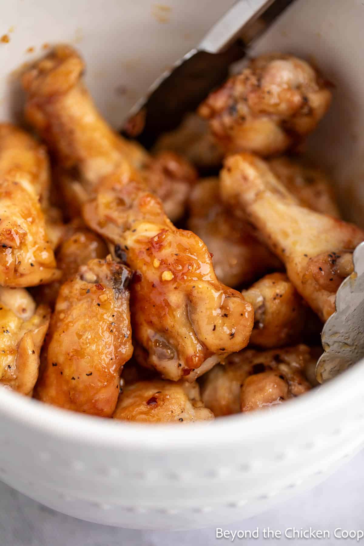 Stirring the chicken wings with a pair of tongs. 