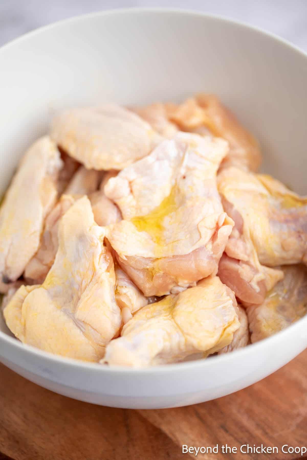 Chicken wings in a bowl with a drizzle of oil over the top of the chicken. 