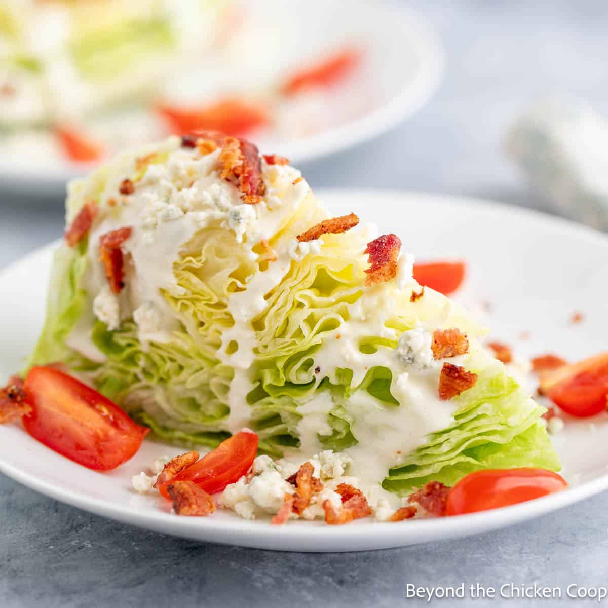 A blue cheese wedge salad with tomatoes and bacon on a white plate. 