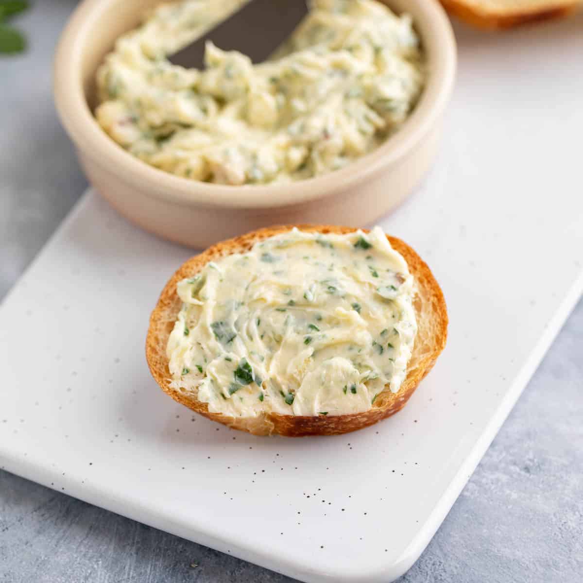 Soft butter with herbs and garlic spread on a small piece of bread.