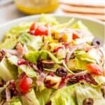 A salad with tomatoes, onions and salami in a white bowl.