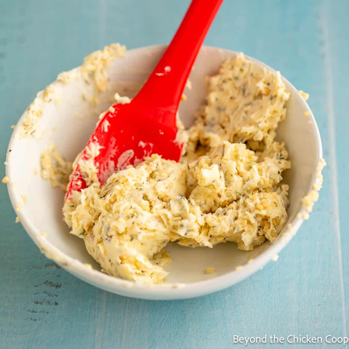Garlic butter in a small bowl with a red spatula. 