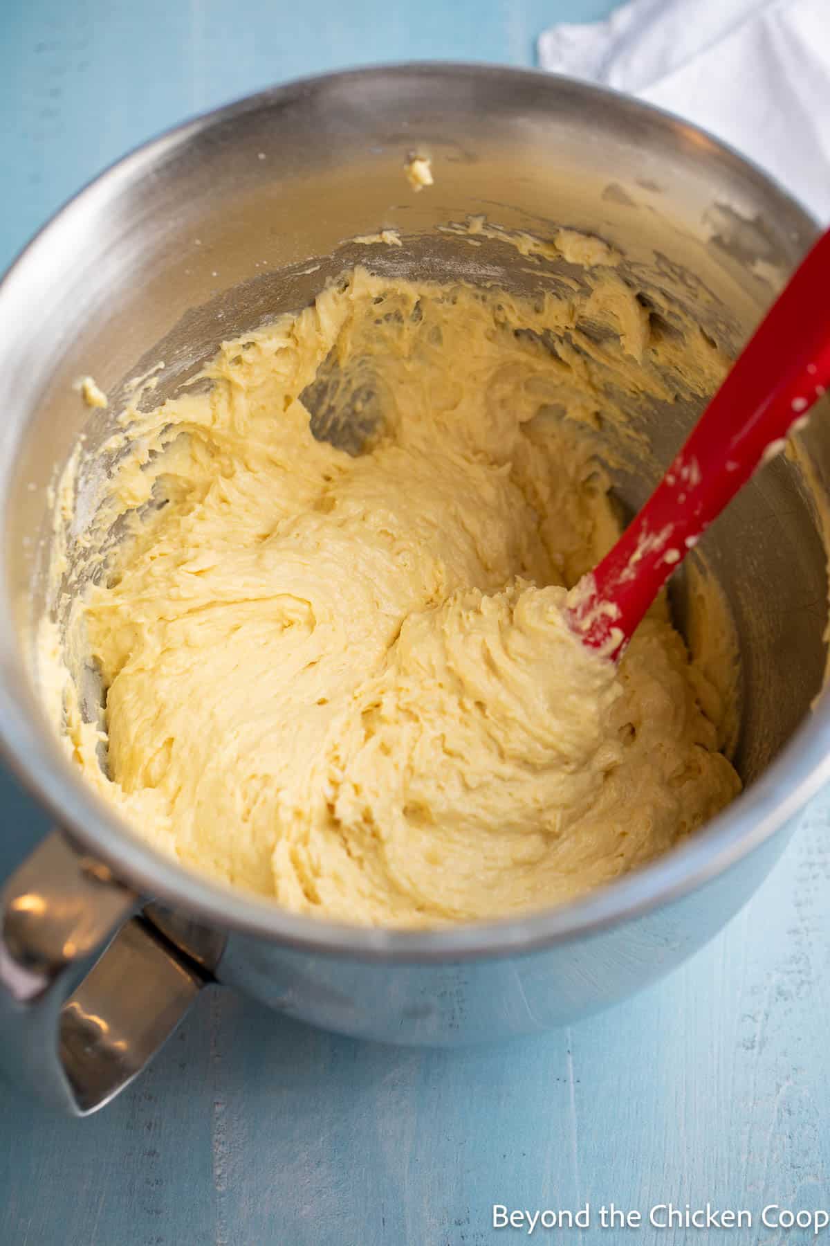 Cake batter in a mixing bowl with a red spatula. 