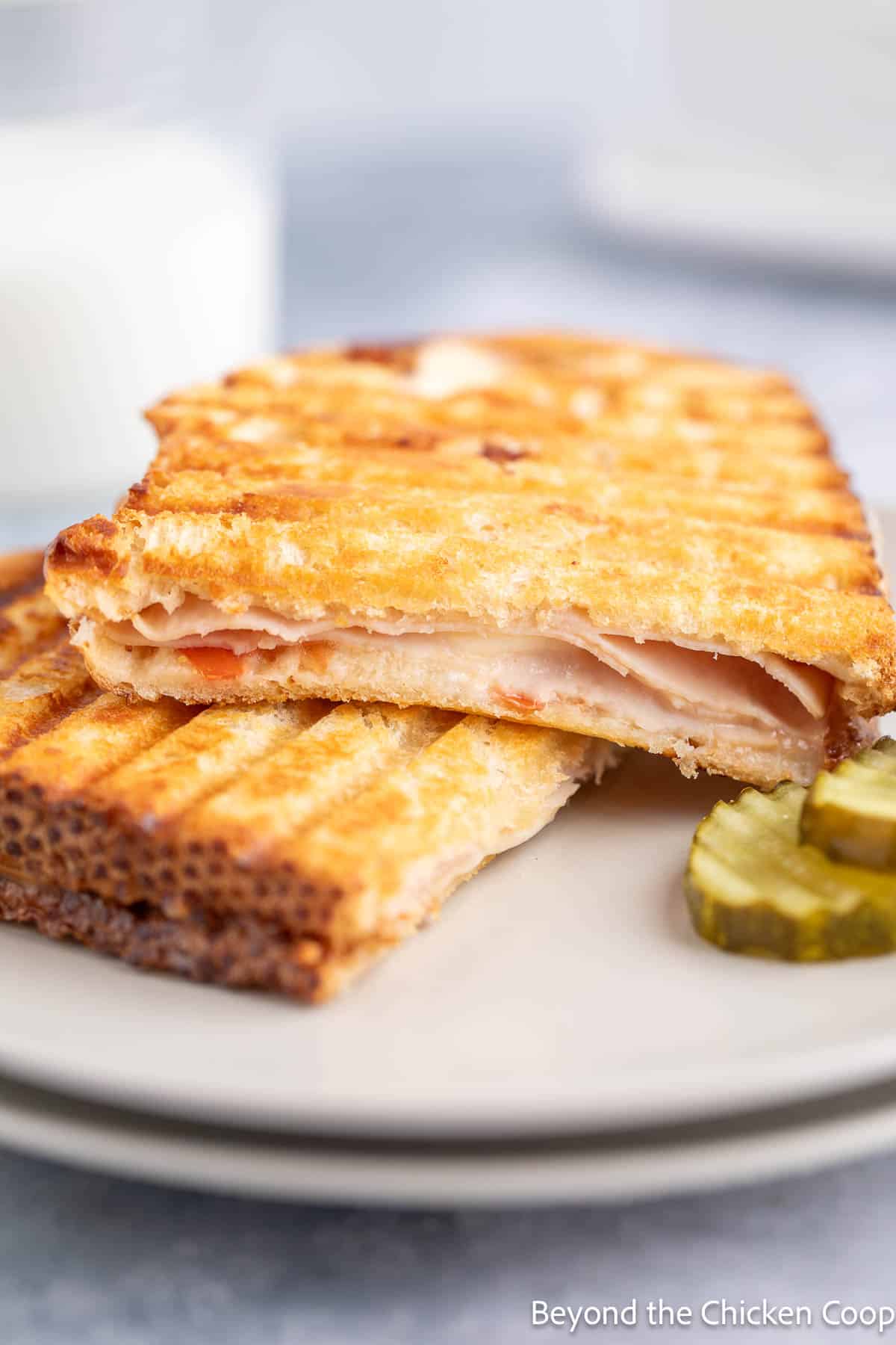 A grilled sandwich filled with turkey and melted cheese on a stack of plates. 
