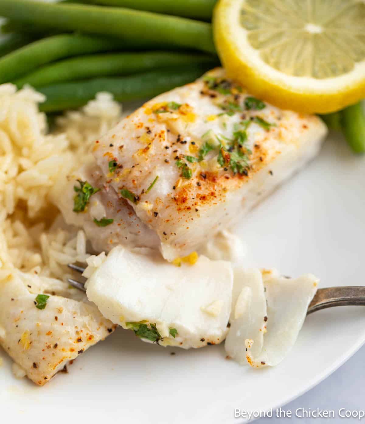 Flaky baked halibut on a plate with green beans and rice. 