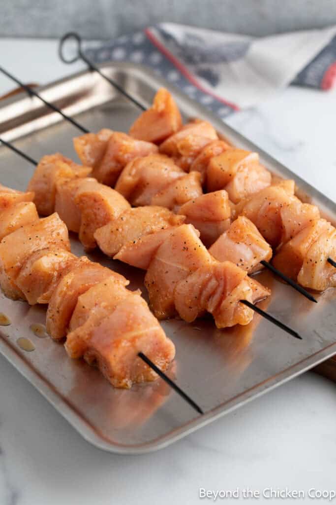 Skewered raw chicken on a baking sheet.