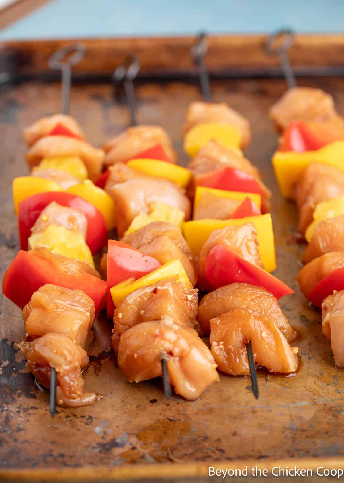 Metal skewers with chicken, peppers and pineapple on each skewer. 