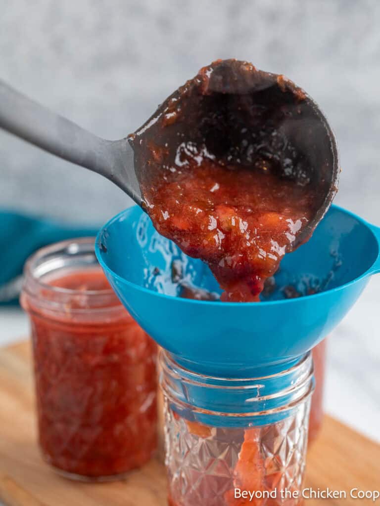Scooping jam into a glass canning jar. 