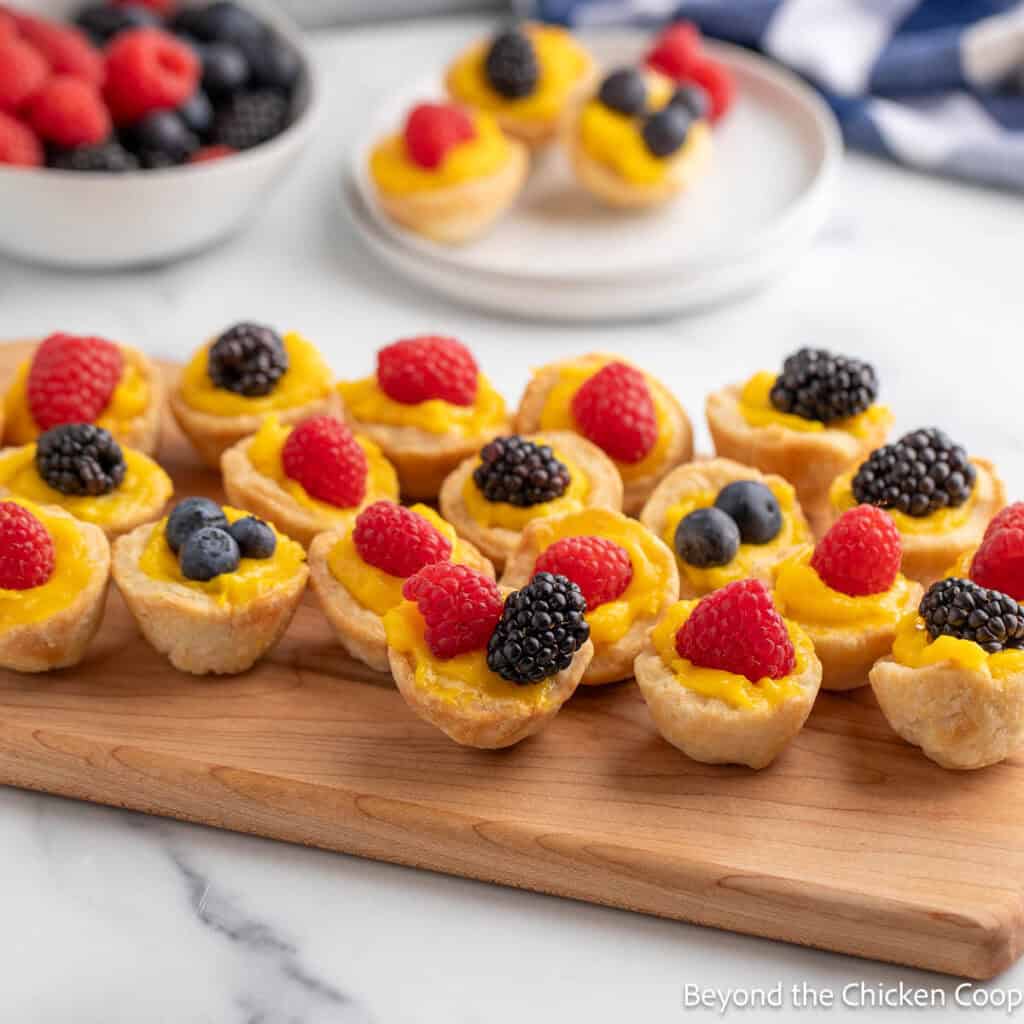 Mini lemon tarts topped with berries on a wooden board.