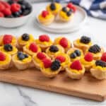 Mini lemon tarts topped with berries on a wooden board.