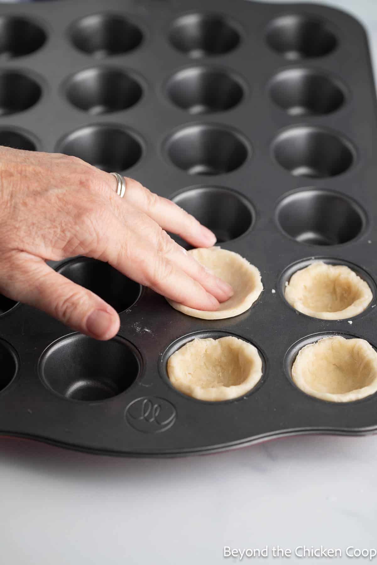 Placing pie crust into a mini muffin tin. 