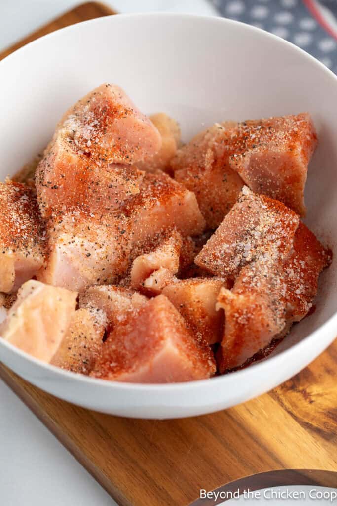 Raw chicken cubes in a bowl with seasoning.