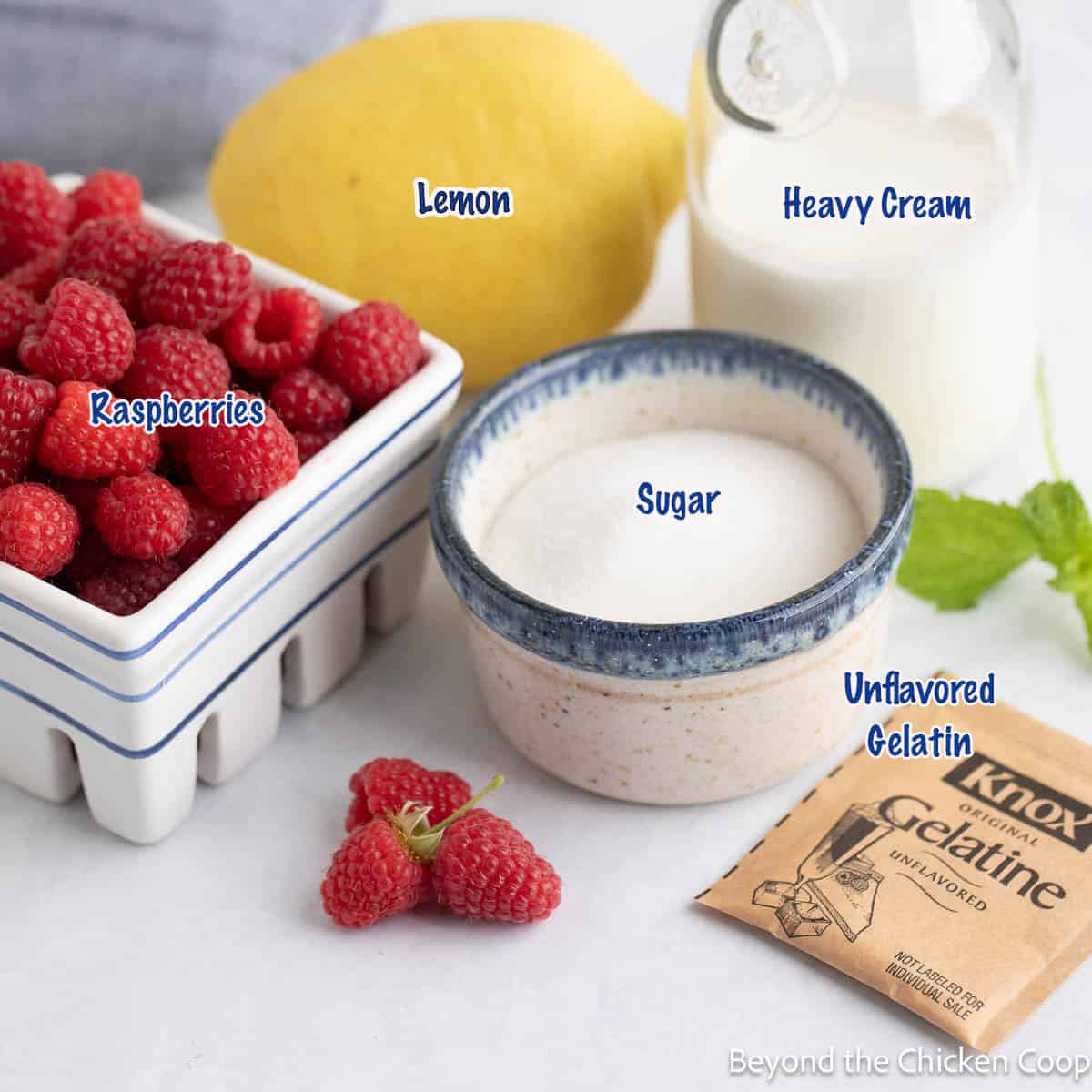 Fresh raspberries, lemon, sugar and cream clustered together on a countertop. 