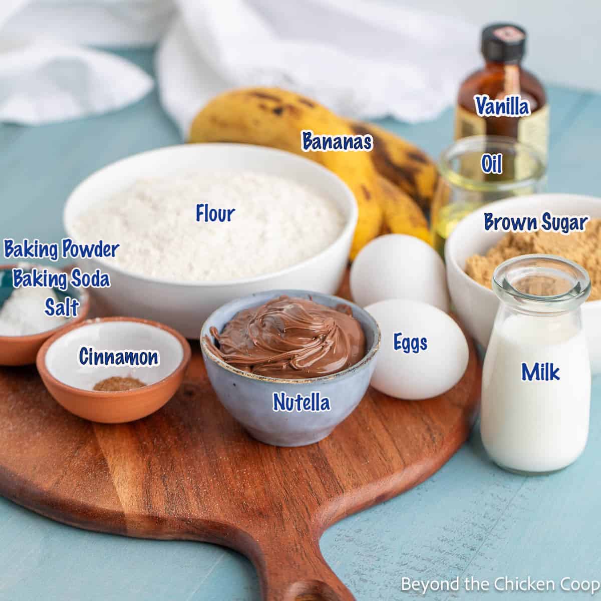 Small bowls filled with flour, sugar, chocolate spread and other ingredients on a board. 