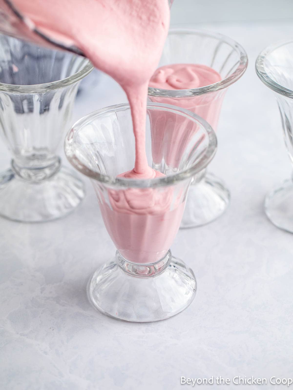 Pouring pink mousse into glass parfaits. 