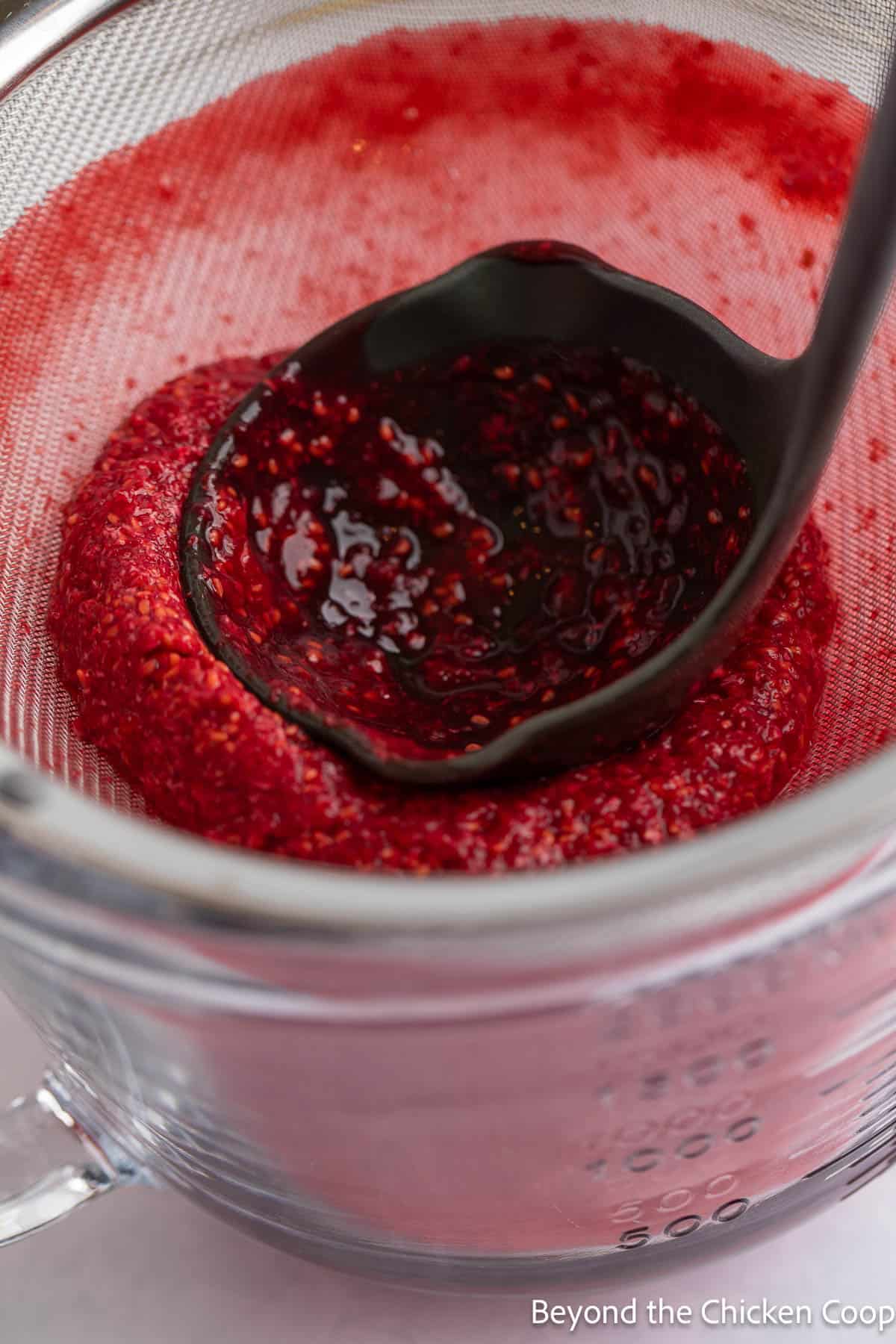 Raspberry puree in a sieve with a soup ladle. 
