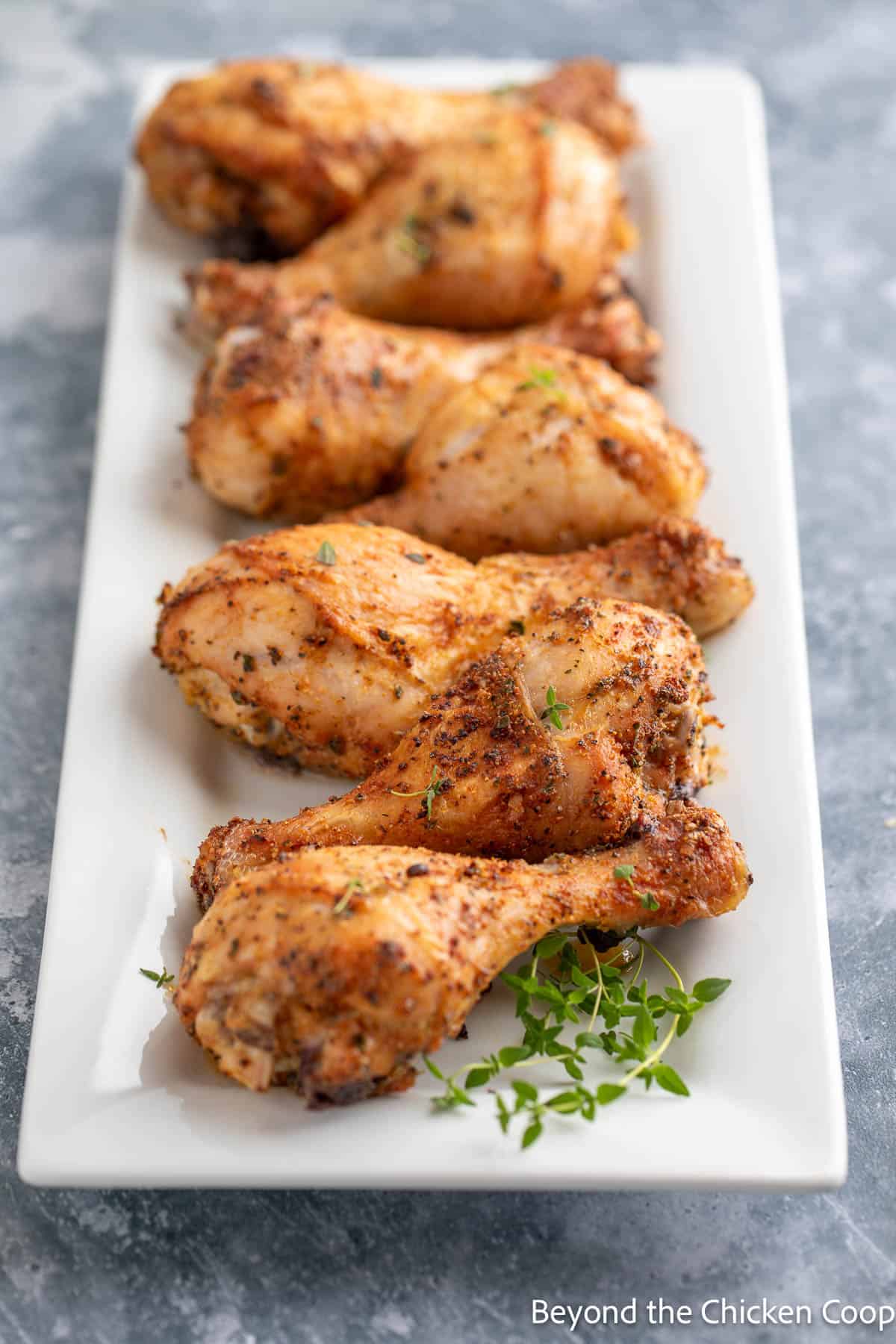 Roasted drumsticks on a platter with fresh herbs. 