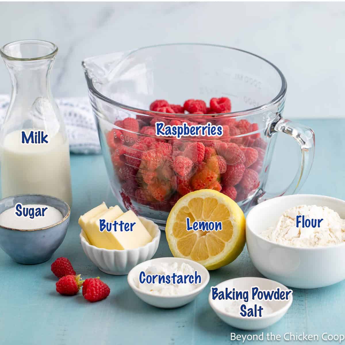 A bowl of fresh raspberries along with ingredients for making a cobbler. 