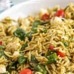 A white bowl filled with pesto covered orzo with tomatoes and spinach.