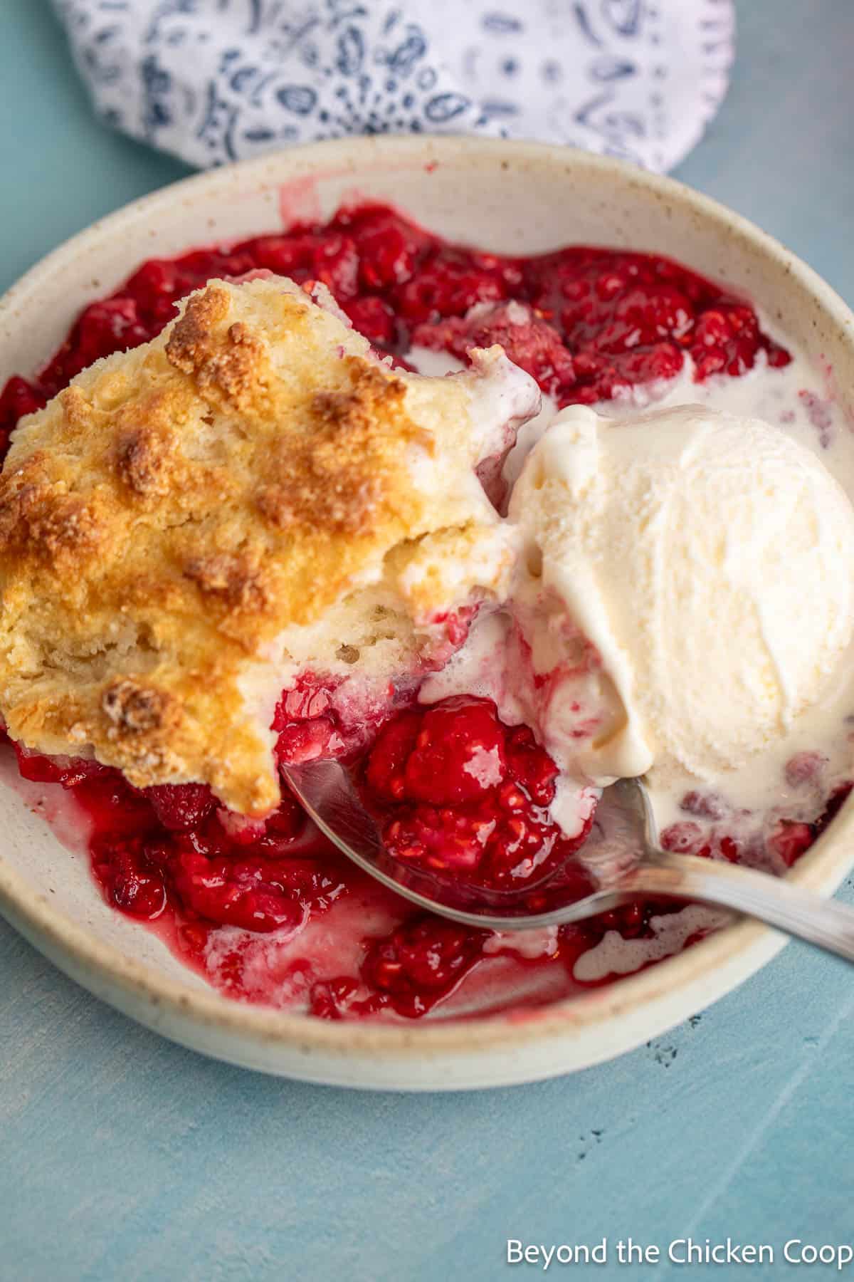 Vanilla ice cream on top of a cobbler with fresh raspberries. 