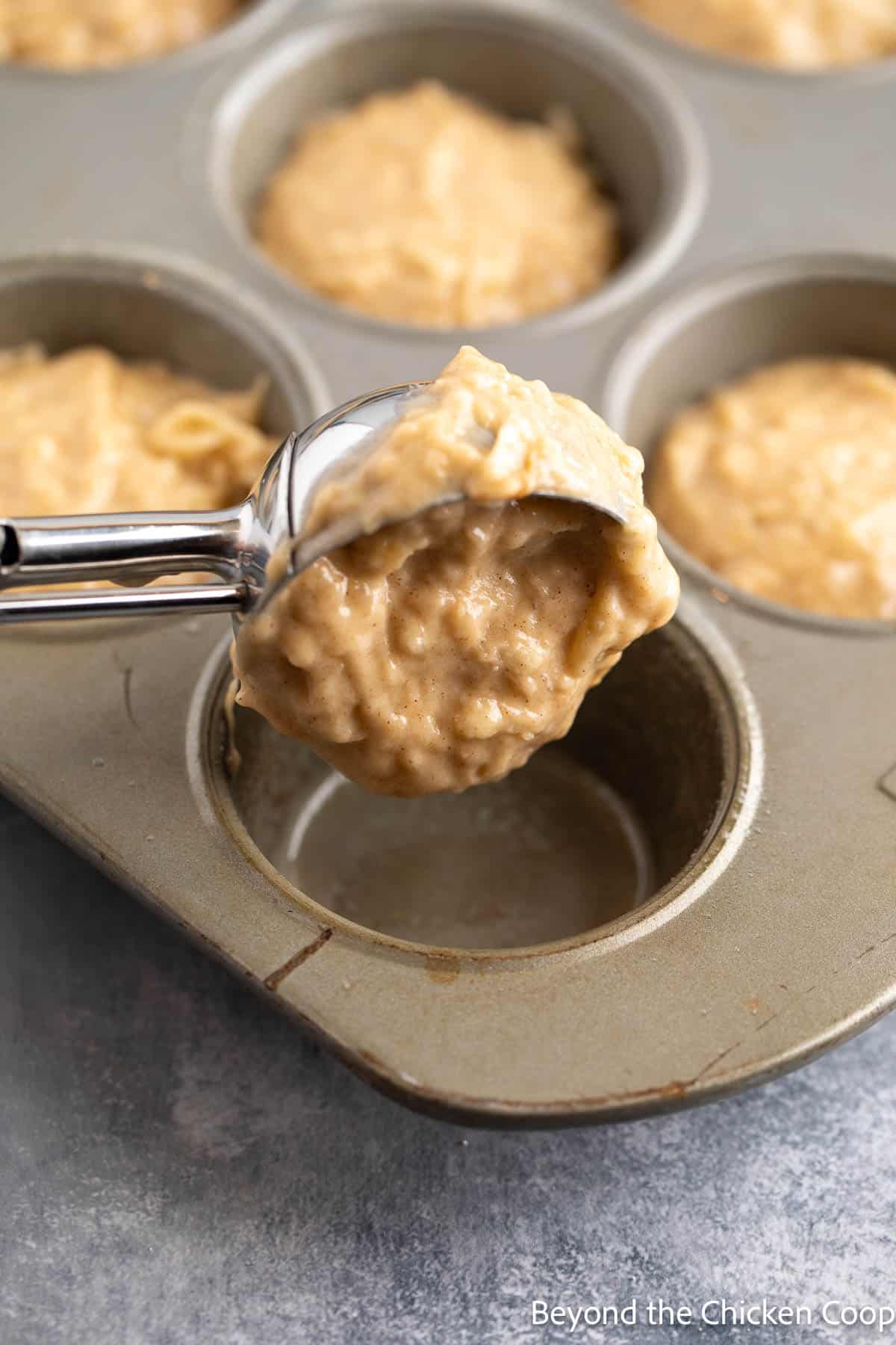 Scooping muffin batter into a muffin tin. 