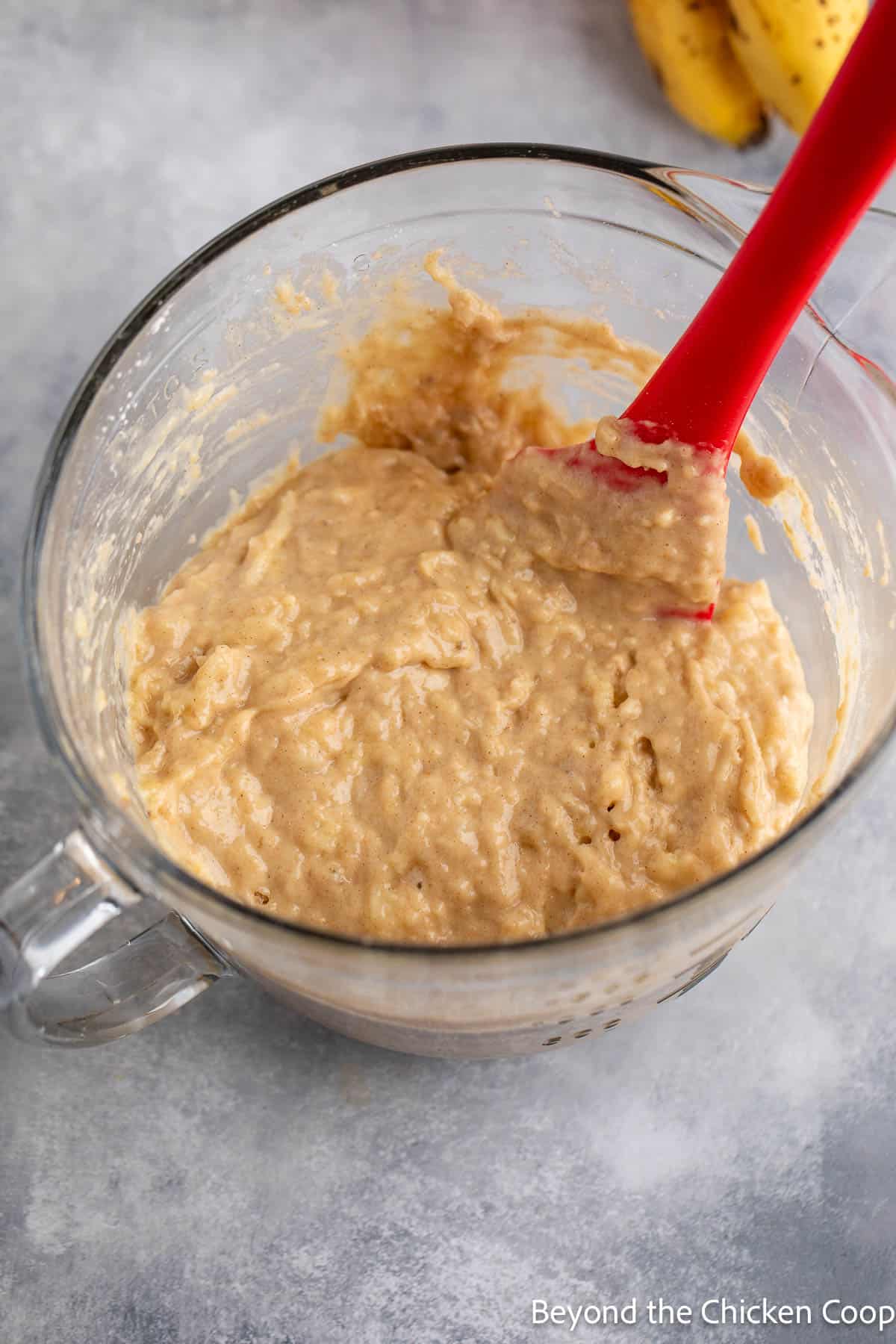 Muffin batter in a mixing bowl with a red spatula. 