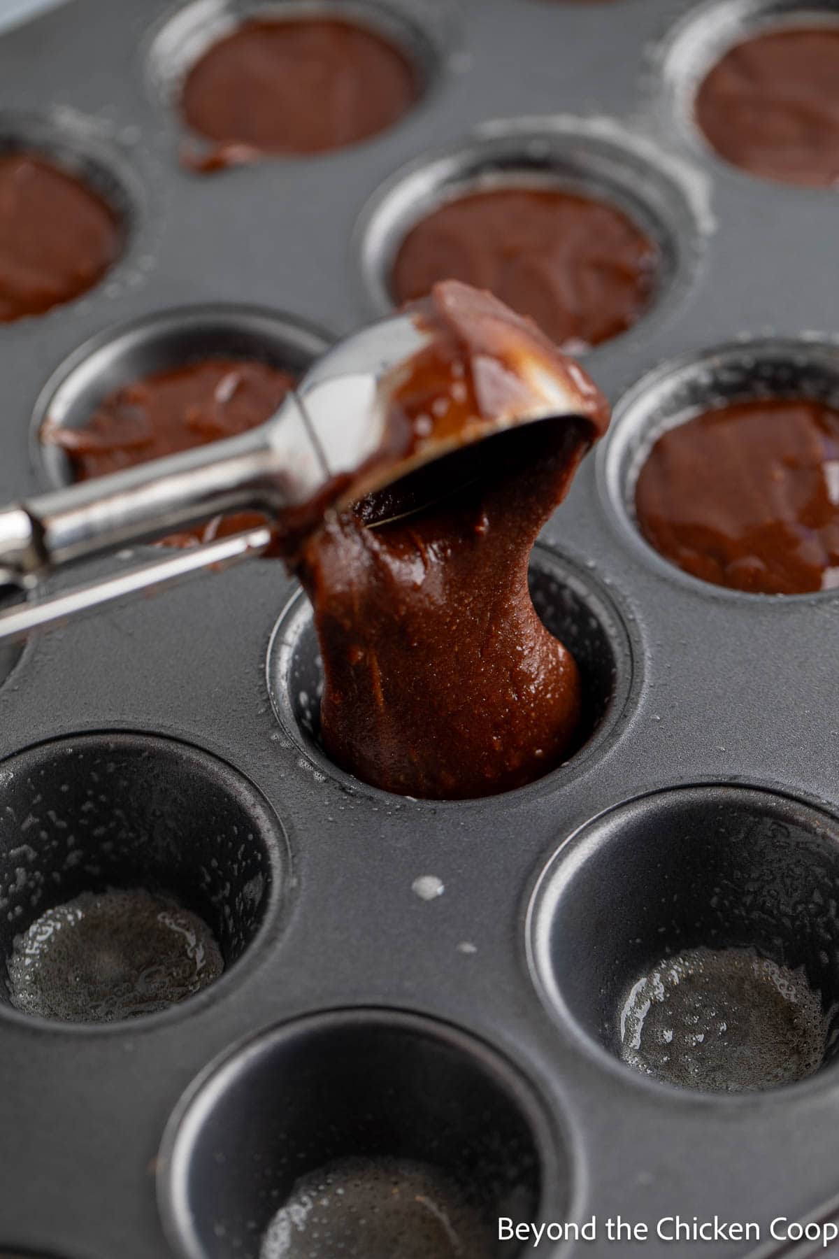 Scooping brownie batter into mini muffin tins. 