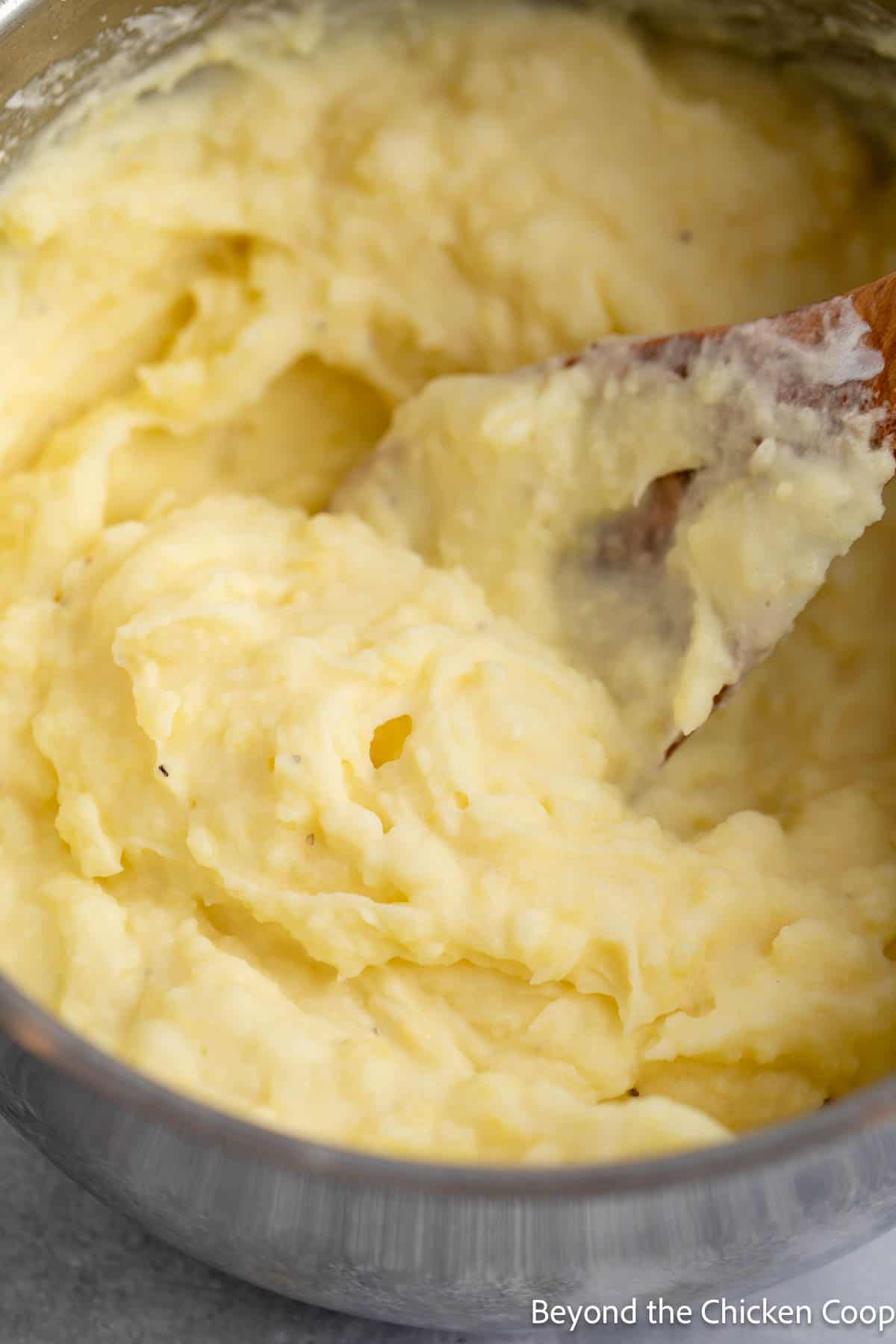 Yukon potatoes mashed in a pot with a wooden spoon. 