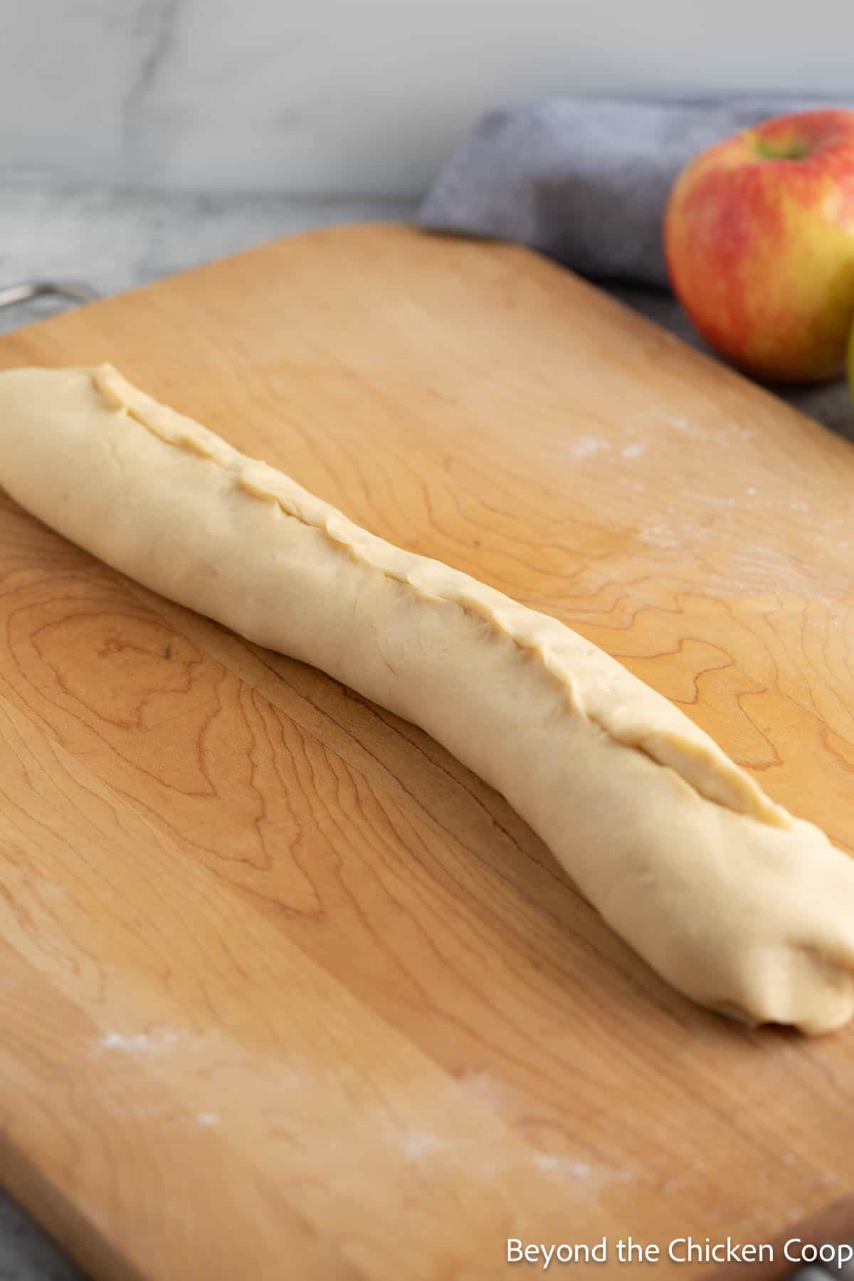 A rolled log of dough on a wooden board. 