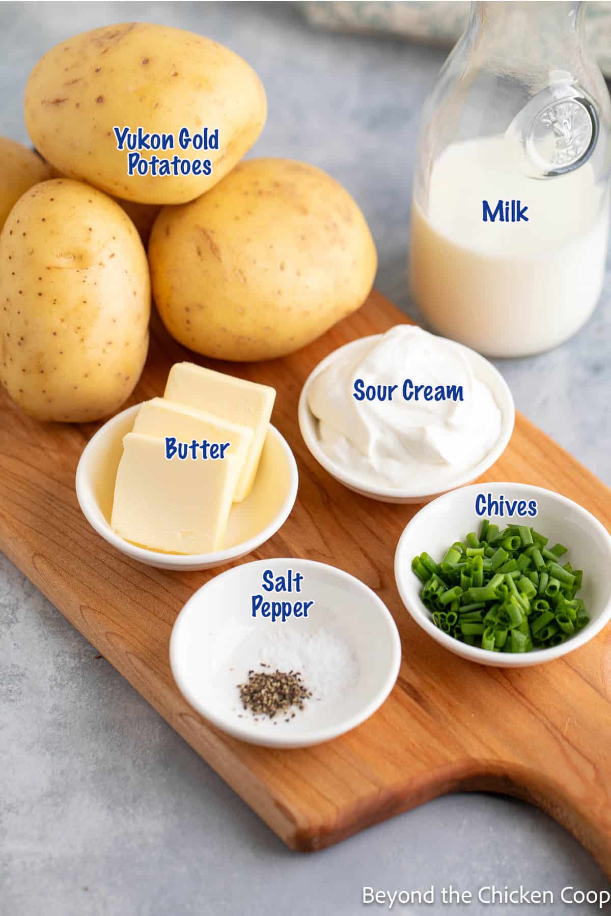 Yukon gold potatoes on a board with small bowls of butter, sour cream and spices. 
