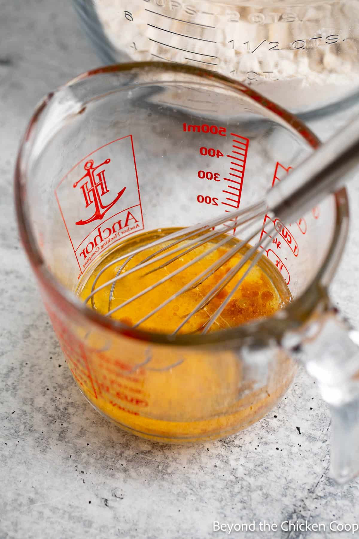 Mixing eggs, oil, and vanilla together in a glass measuring cup with a small whisk. 