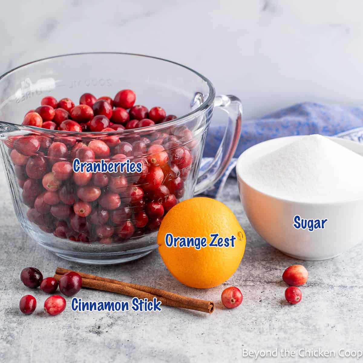 A bowl filled with fresh cranberries next to a bowl of sugar an an orange. 