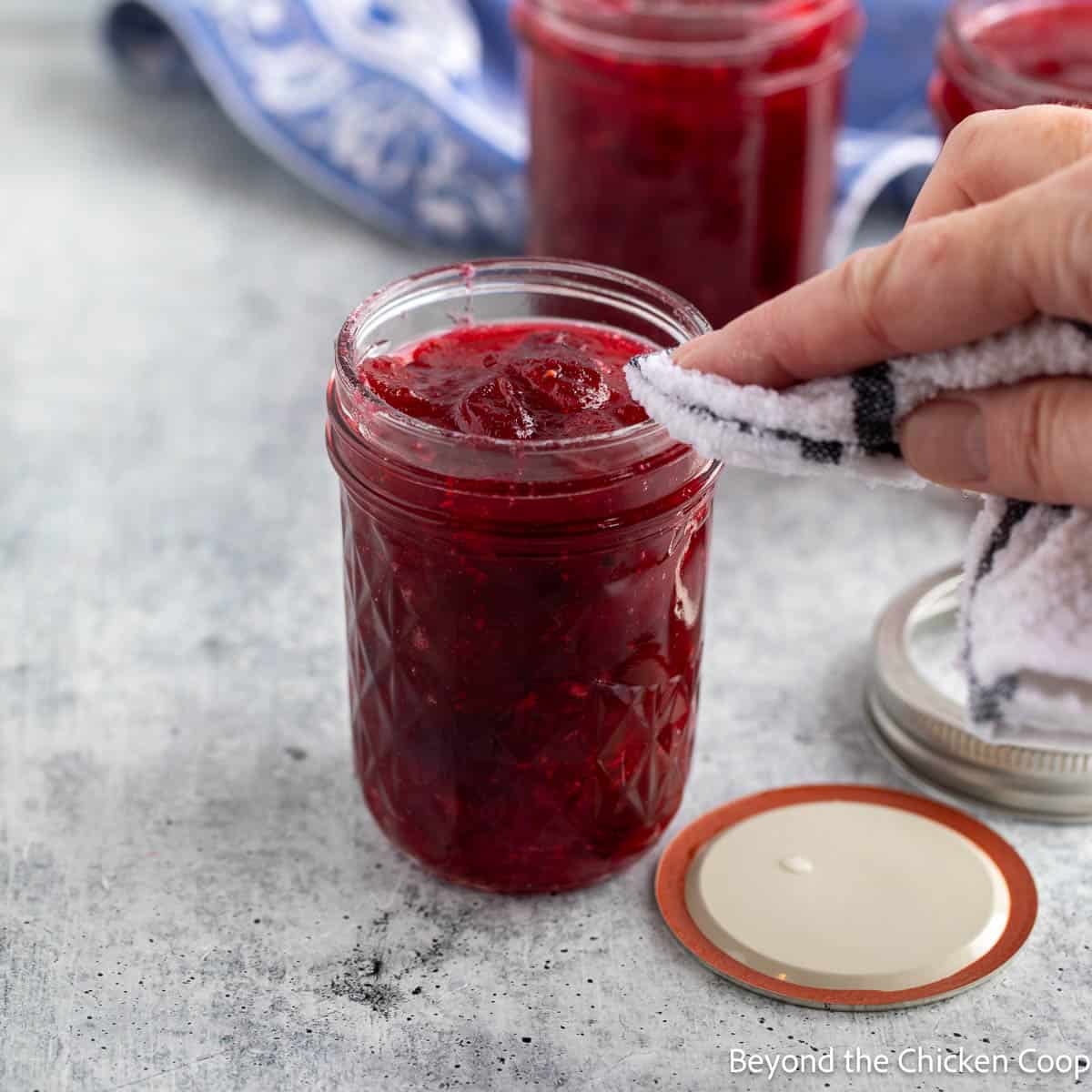 Wiping the rim of a canning jar filled with red sauce. 