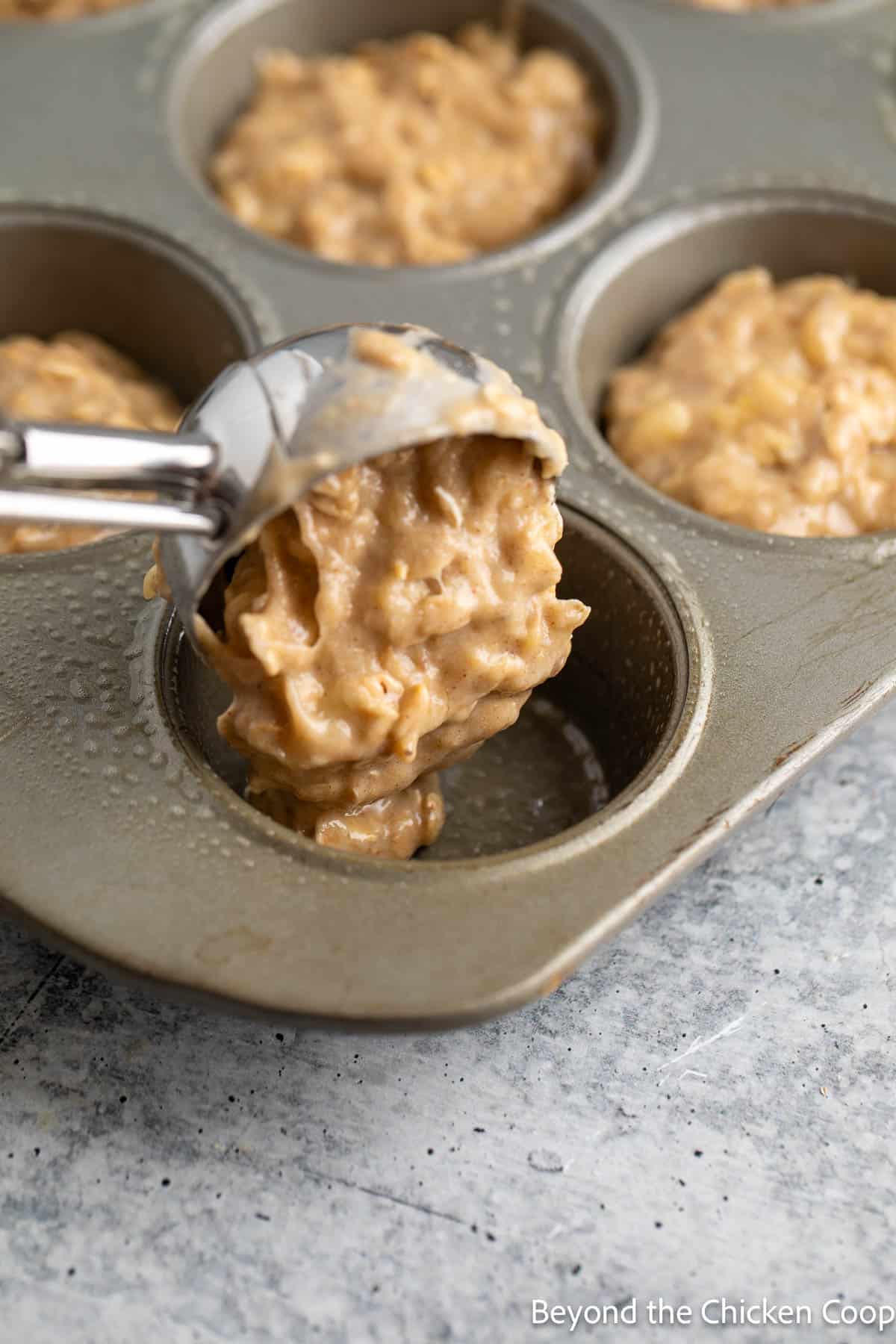 Scooping muffin batter into a muffin tin. 