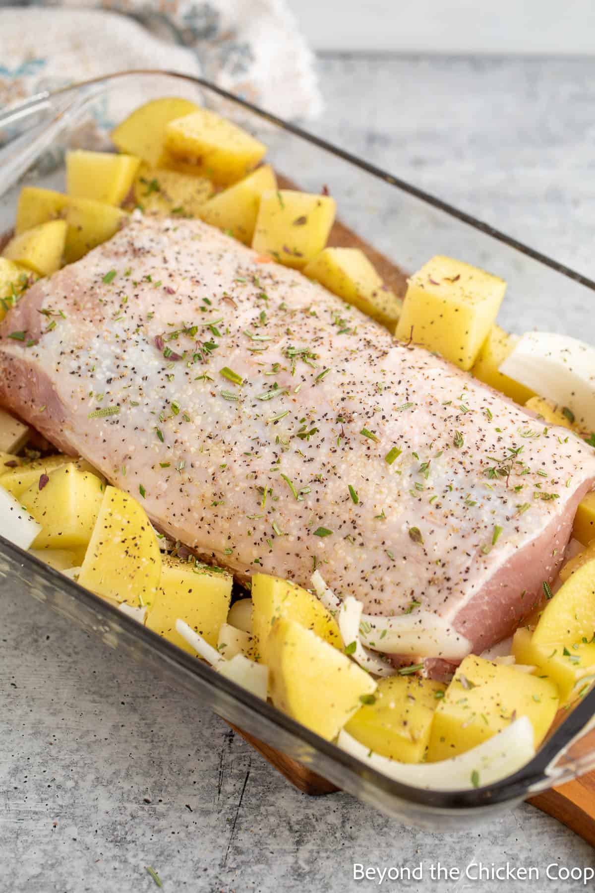 Seasoned pork loin in a baking dish with potatoes and onions. 