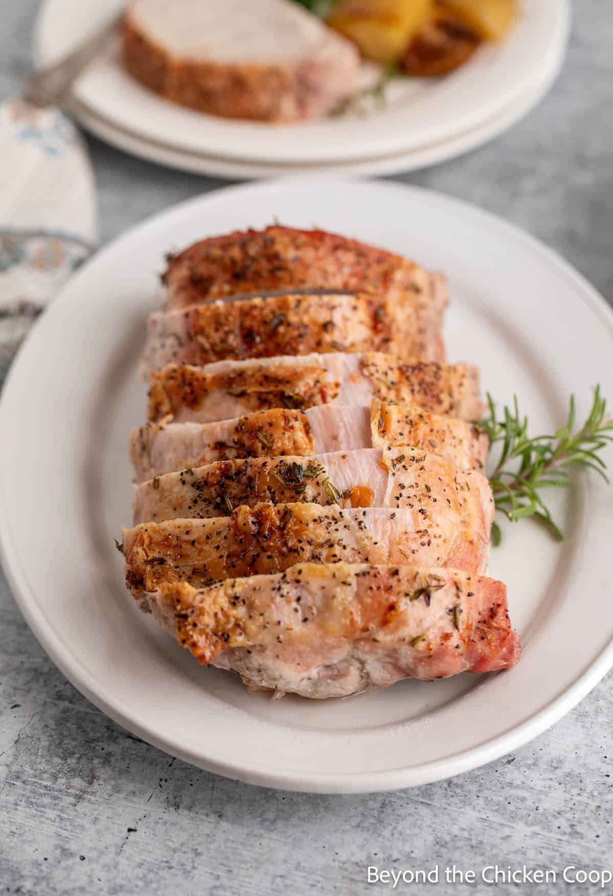 Sliced pork loin on a white platter with fresh rosemary. 