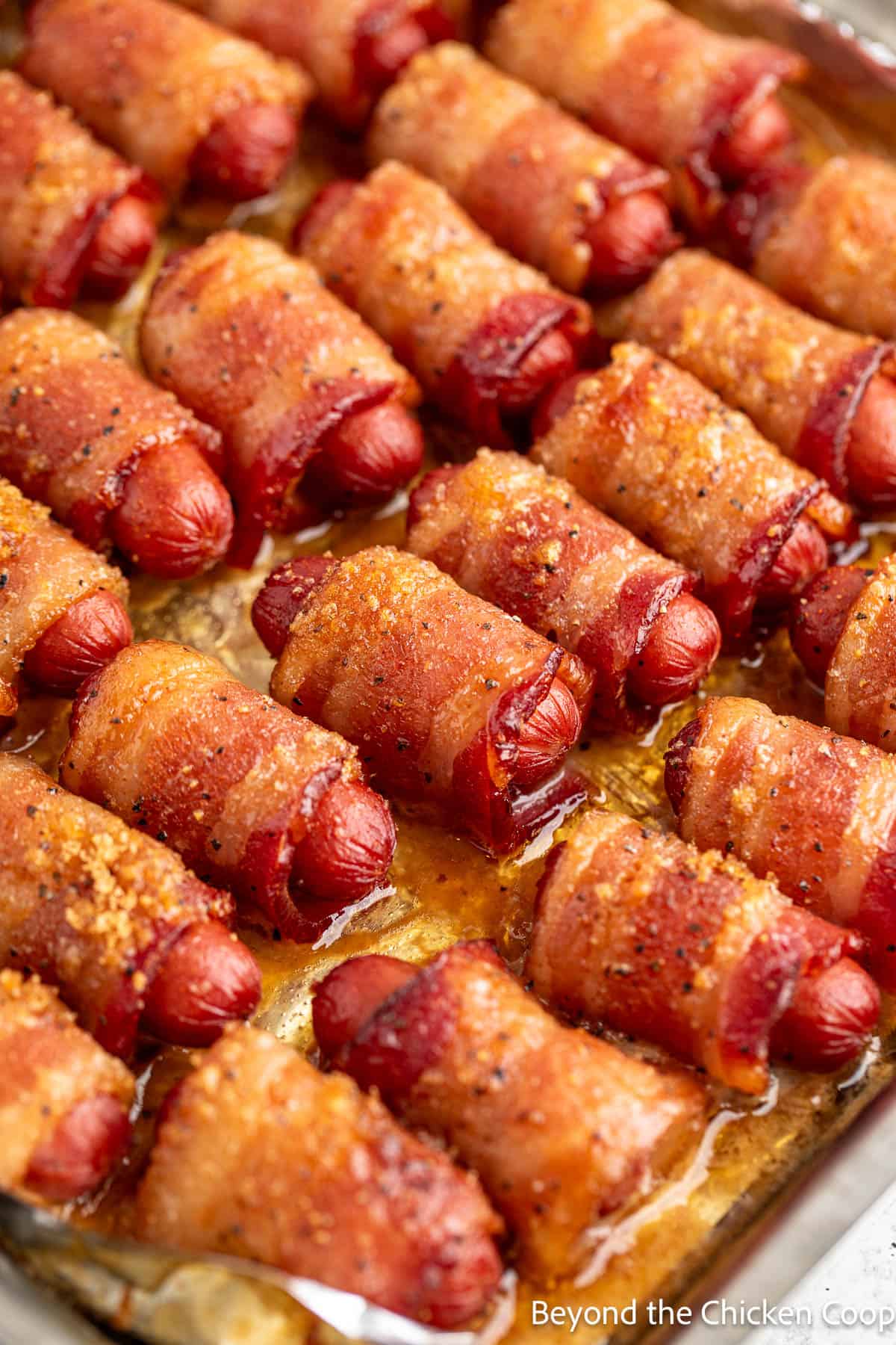 Baked little smokies wrapped with bacon on a baking sheet. 