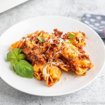 Baked tortellini with meat and sauce on a white plate.