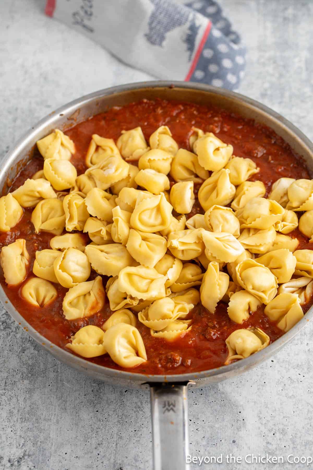 Fresh tortellini added to a skillet with sauce. 