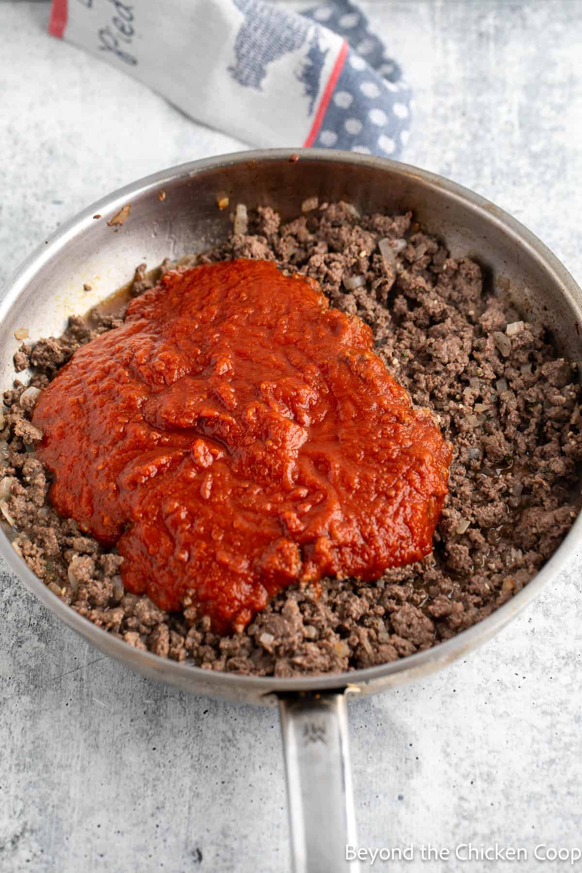 Tomato sauce on browned burger in a skillet. 