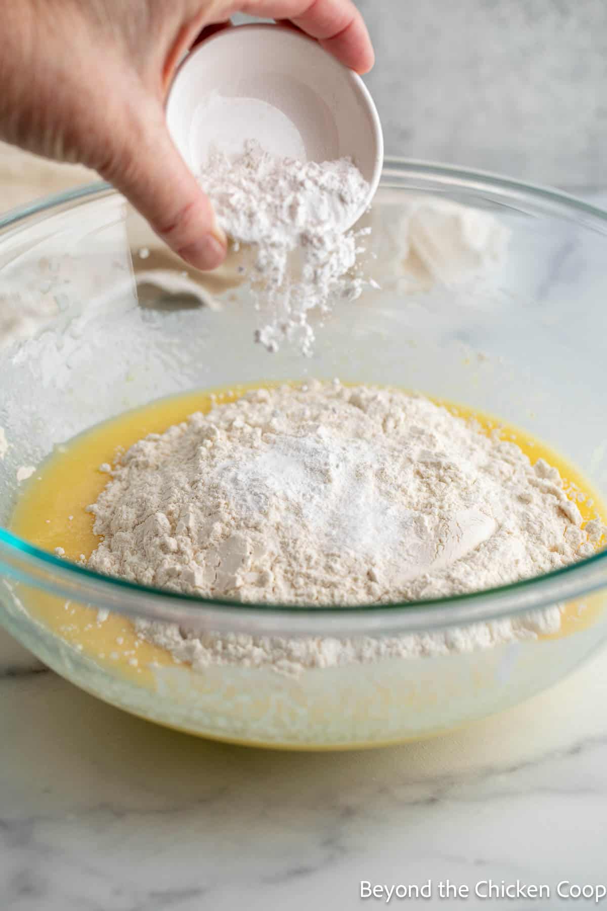 Sprinkling baking powder over flour in a bowl. 