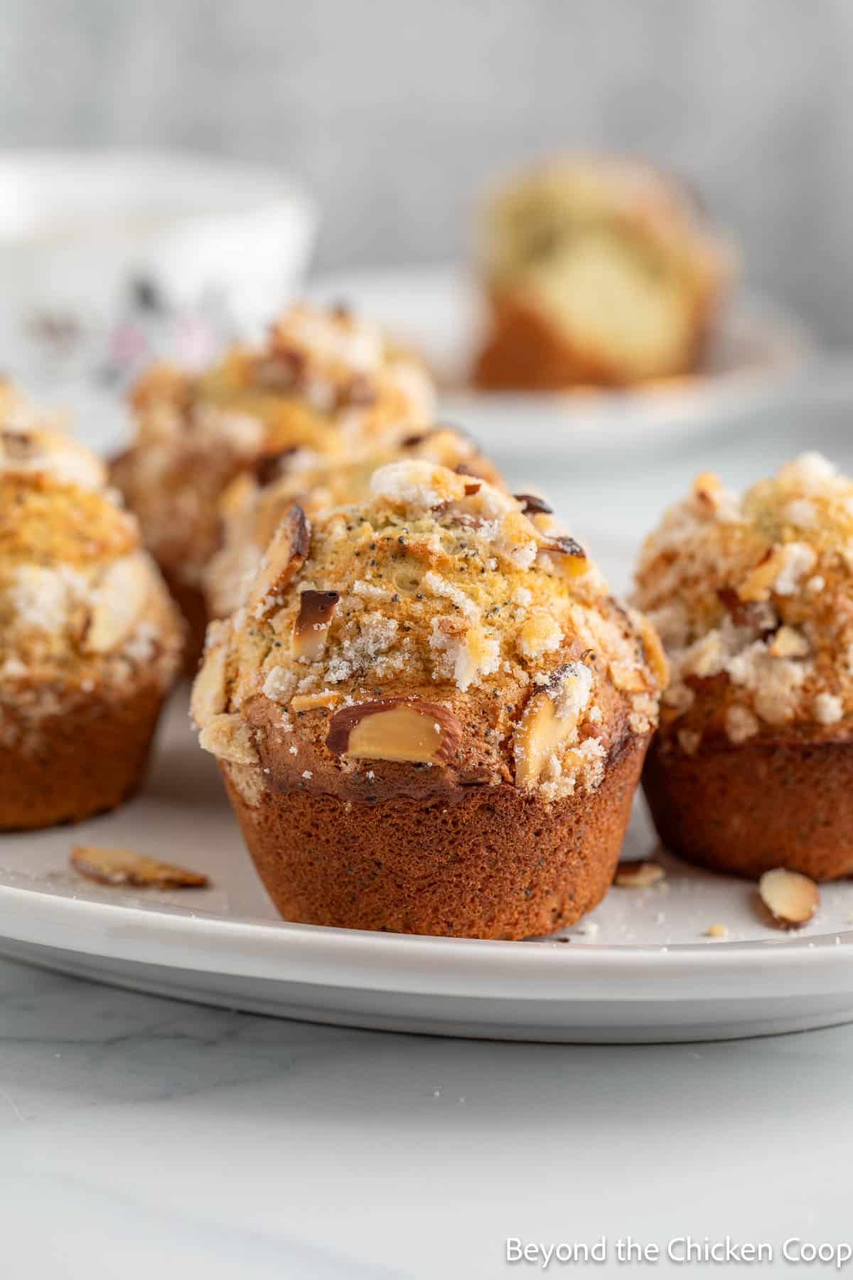 Muffins topped with sliced almonds on a white platter. 
