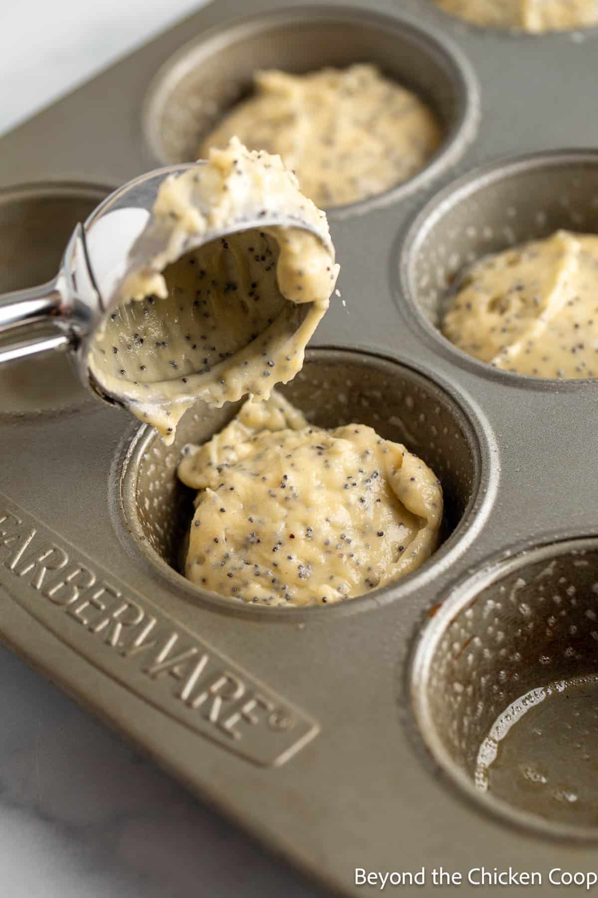 Scooping muffin batter into a muffin tin. 