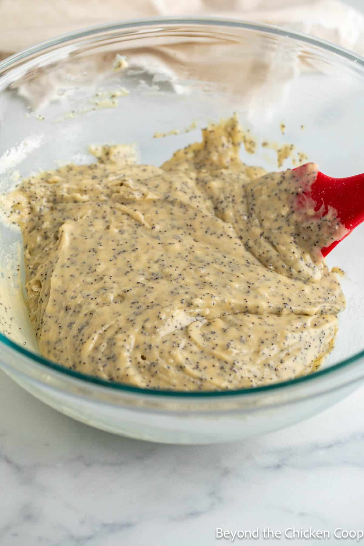 Muffin batter mixed in a glass bowl with a red spatula. 